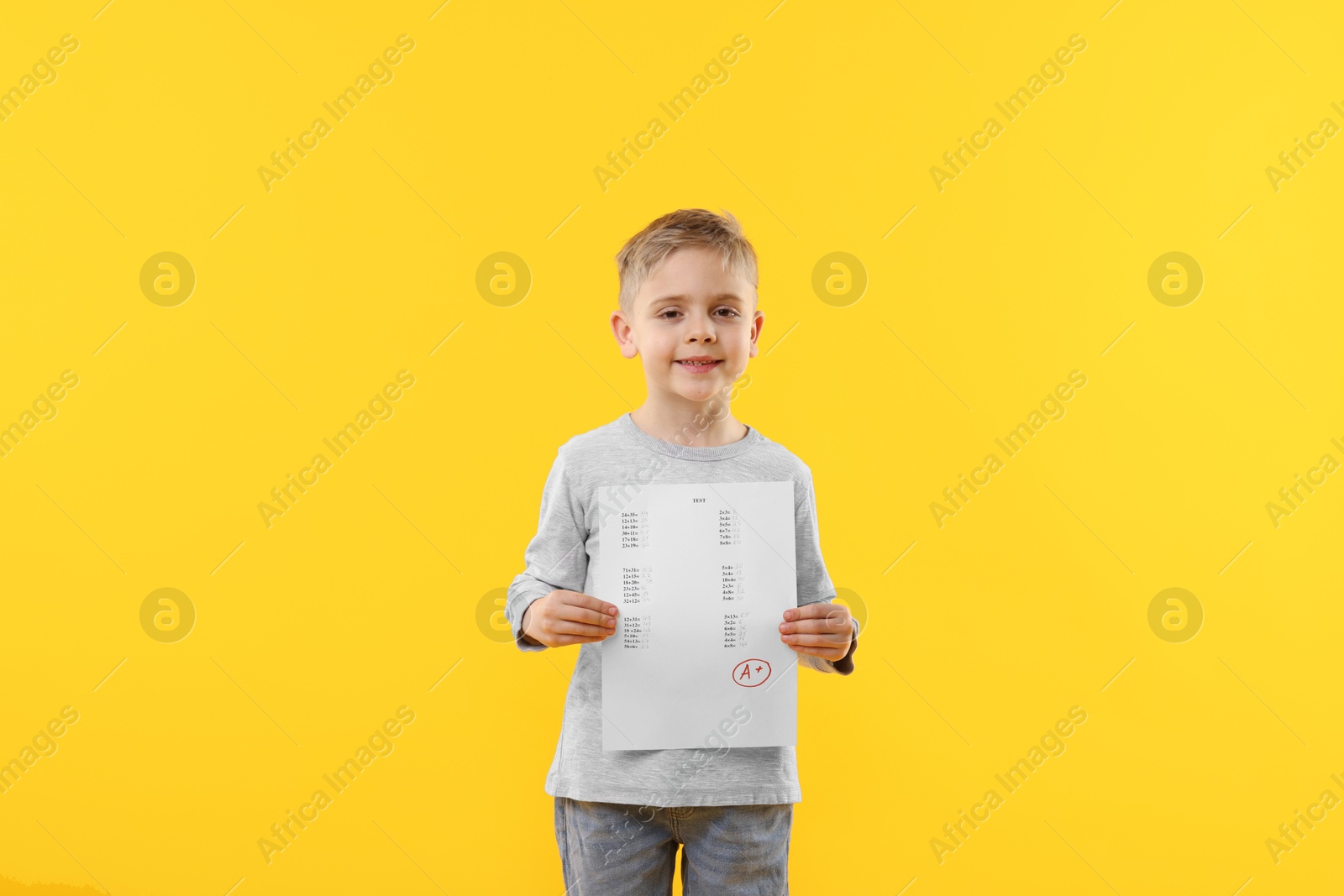 School grade. Little boy holding answer sheet with letter A and plus symbol on yellow background Photo of School grade. Little boy holding answer sheet with letter A and plus symbol on yellow background