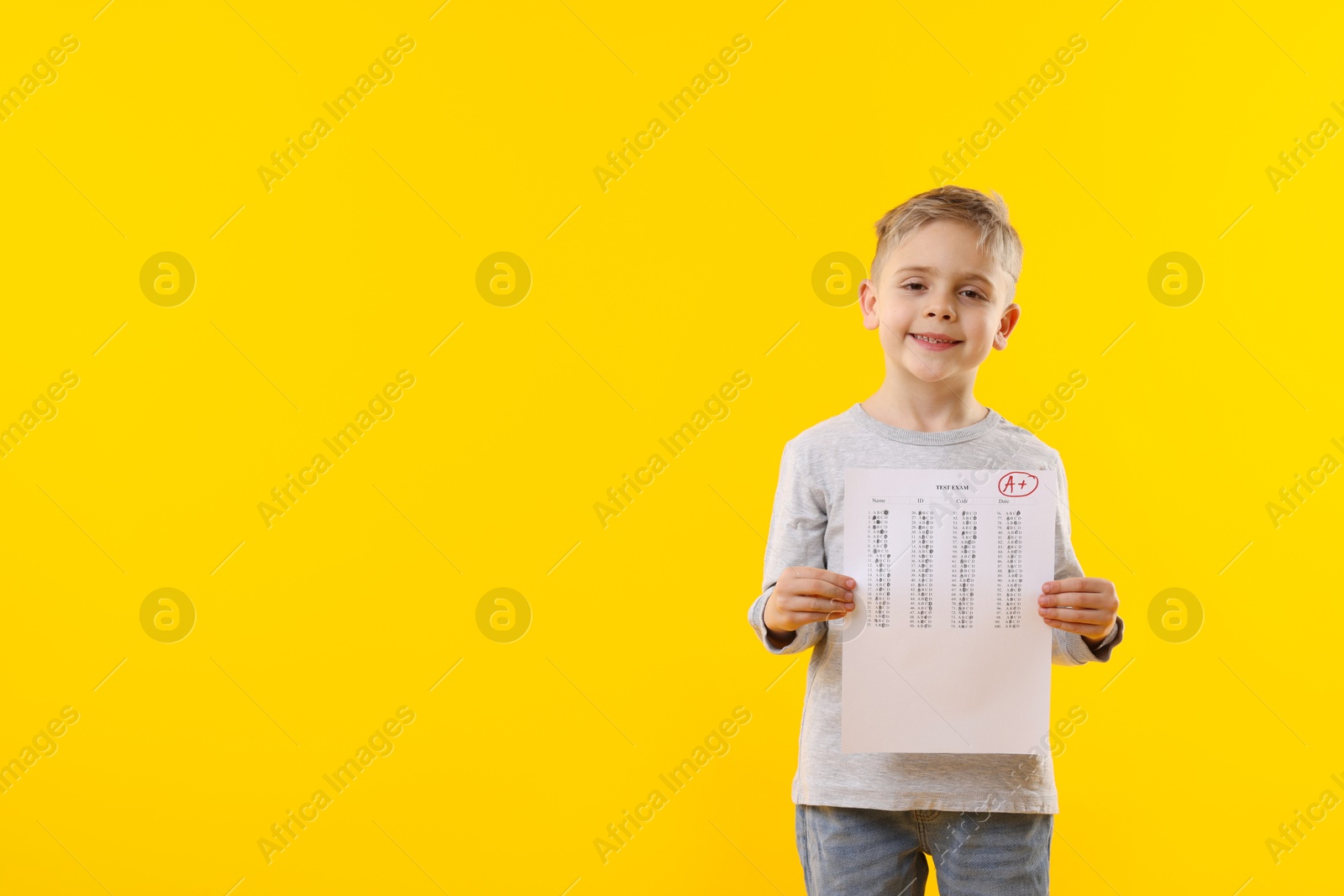 School grade. Little boy holding answer sheet with letter A and plus symbol on yellow background, space for text Photo of School grade. Little boy holding answer sheet with letter A and plus symbol on yellow background, space for text