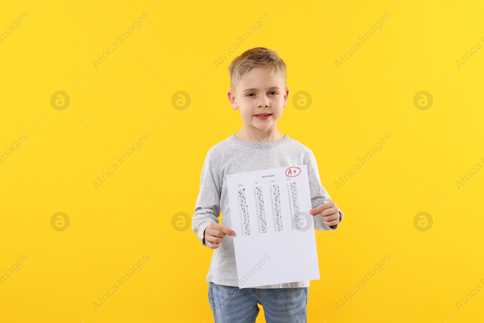 School grade. Little boy holding answer sheet with letter A and plus symbol on yellow background Photo of School grade. Little boy holding answer sheet with letter A and plus symbol on yellow background