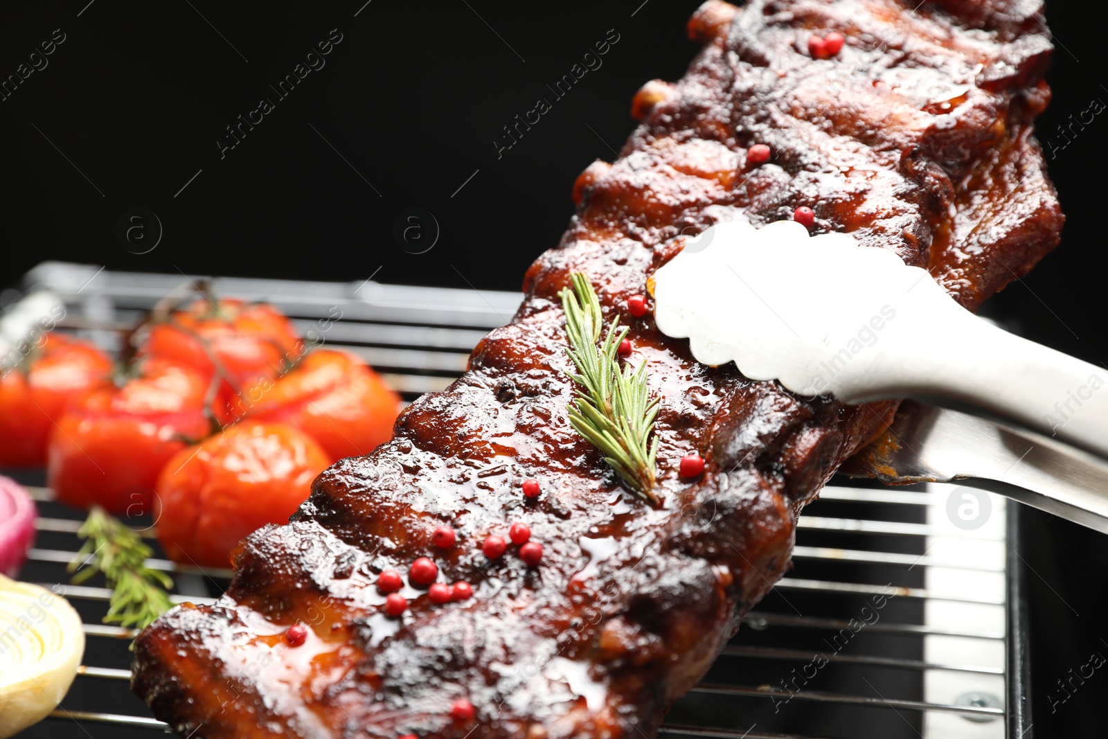 Photo of Taking delicious roasted pork ribs with tongs from grill, closeup