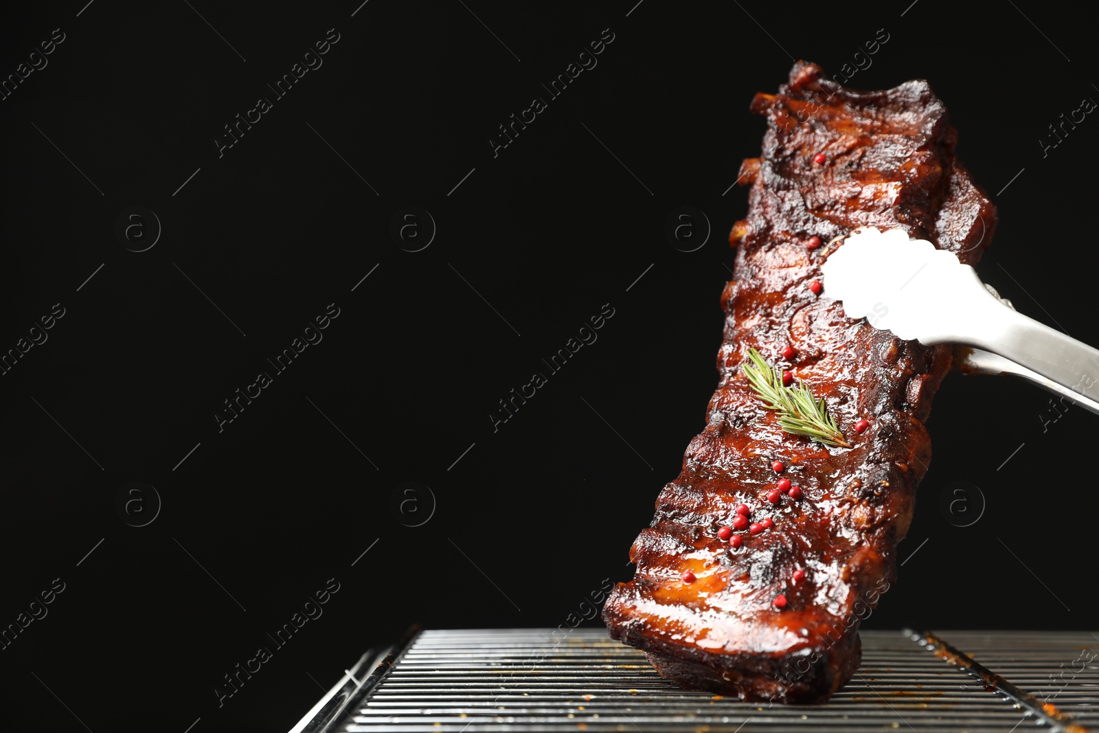 Taking delicious roasted pork ribs with tongs from grill on black background, closeup. Space for text Photo of Taking delicious roasted pork ribs with tongs from grill on black background, closeup. Space for text