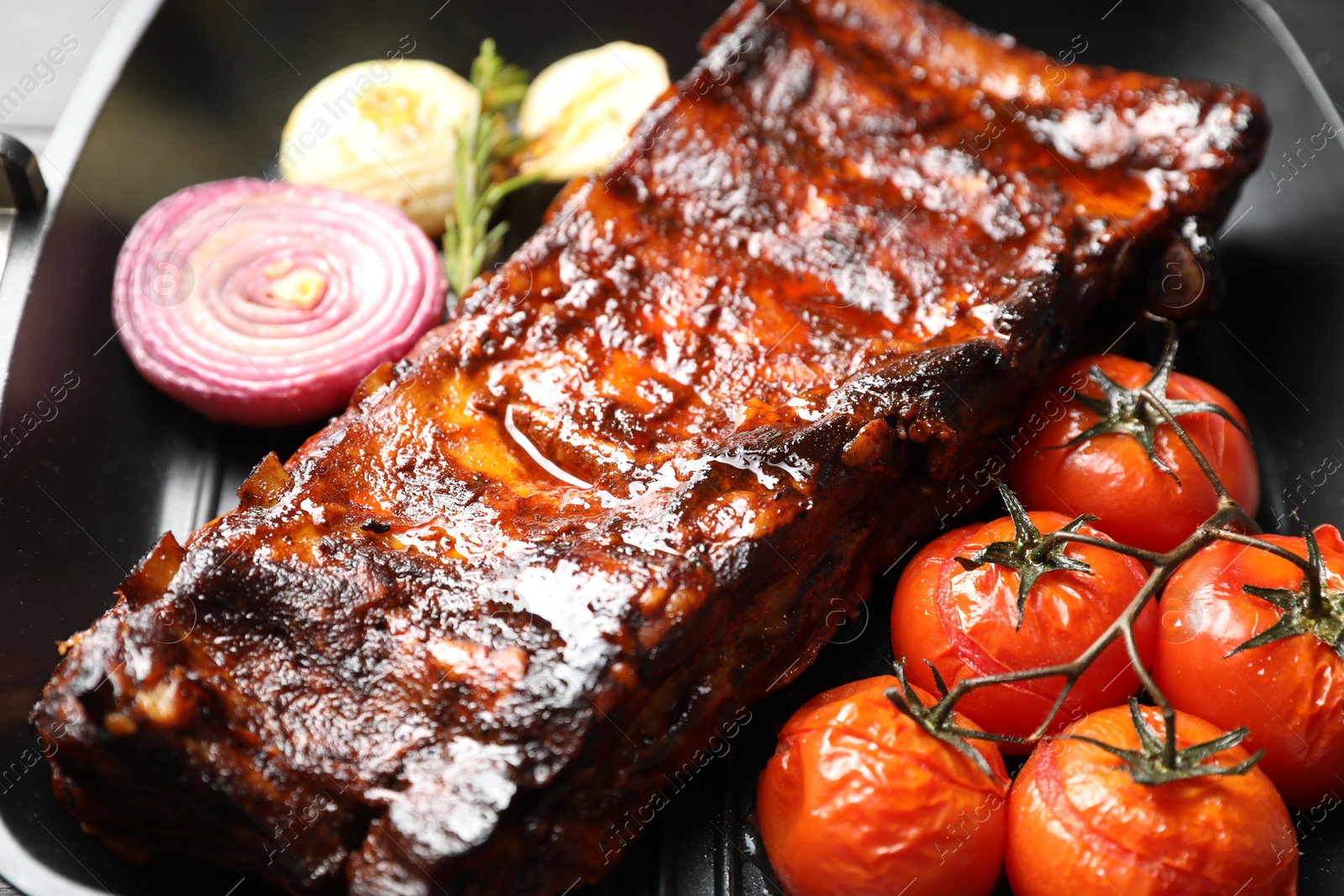 Delicious roasted pork ribs with tomatoes and onions on grill pan, closeup Photo of Delicious roasted pork ribs with tomatoes and onions on grill pan, closeup
