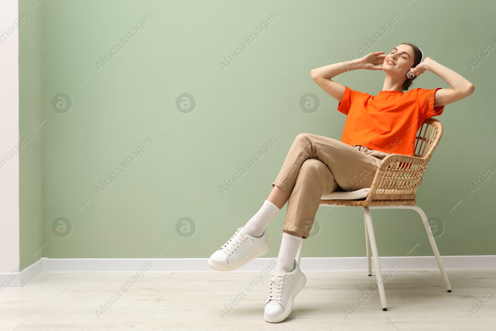 Beautiful woman with headphones relaxing in comfortable armchair near pale green wall indoors, space for text Photo of Beautiful woman with headphones relaxing in comfortable armchair near pale green wall indoors, space for text