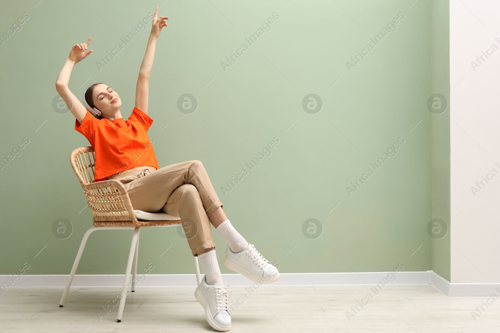 Beautiful woman with headphones relaxing in comfortable armchair near pale green wall indoors, space for text Photo of Beautiful woman with headphones relaxing in comfortable armchair near pale green wall indoors, space for text