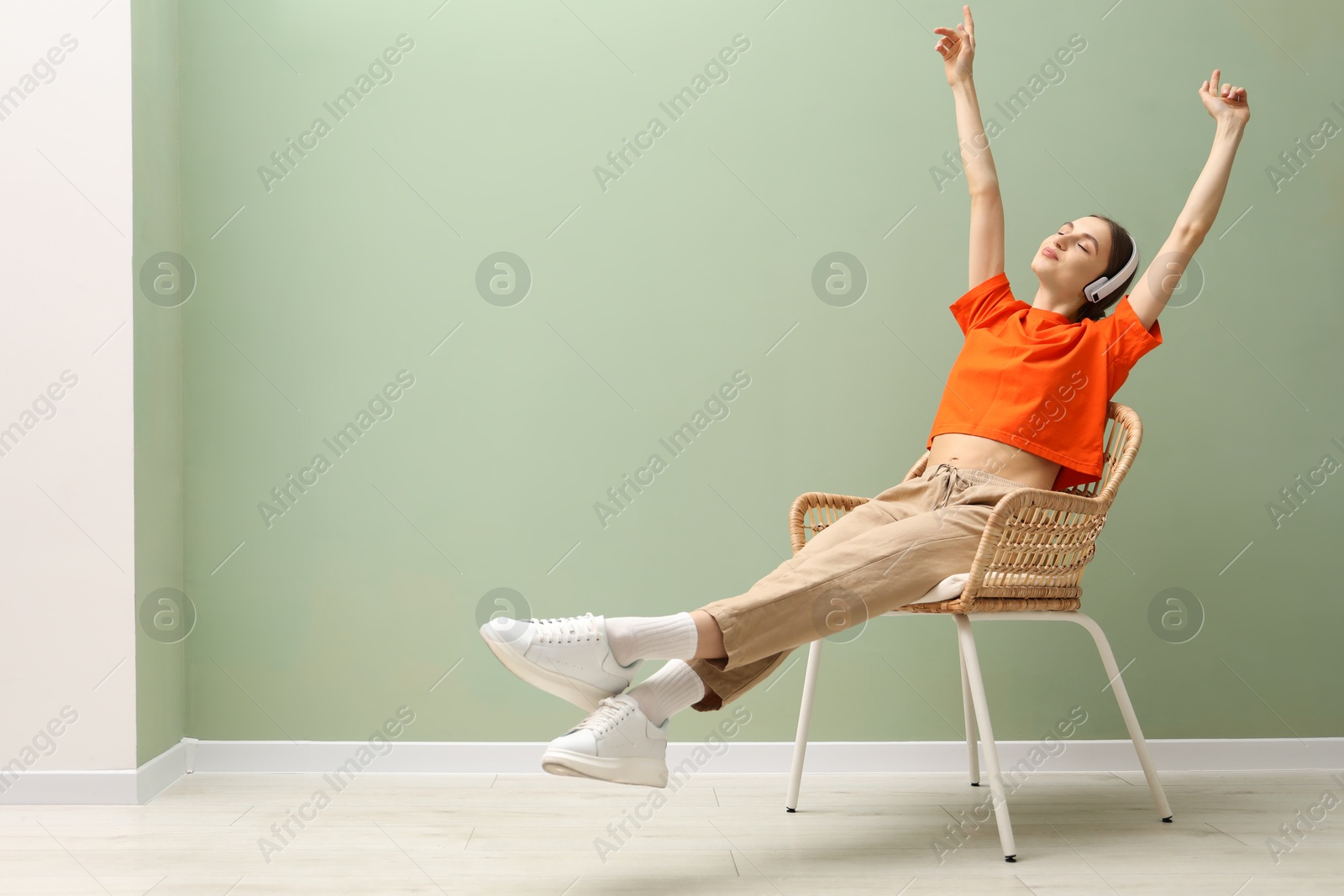 Beautiful woman with headphones relaxing in comfortable wicker armchair near pale green wall indoors, space for text Photo of Beautiful woman with headphones relaxing in comfortable wicker armchair near pale green wall indoors, space for text