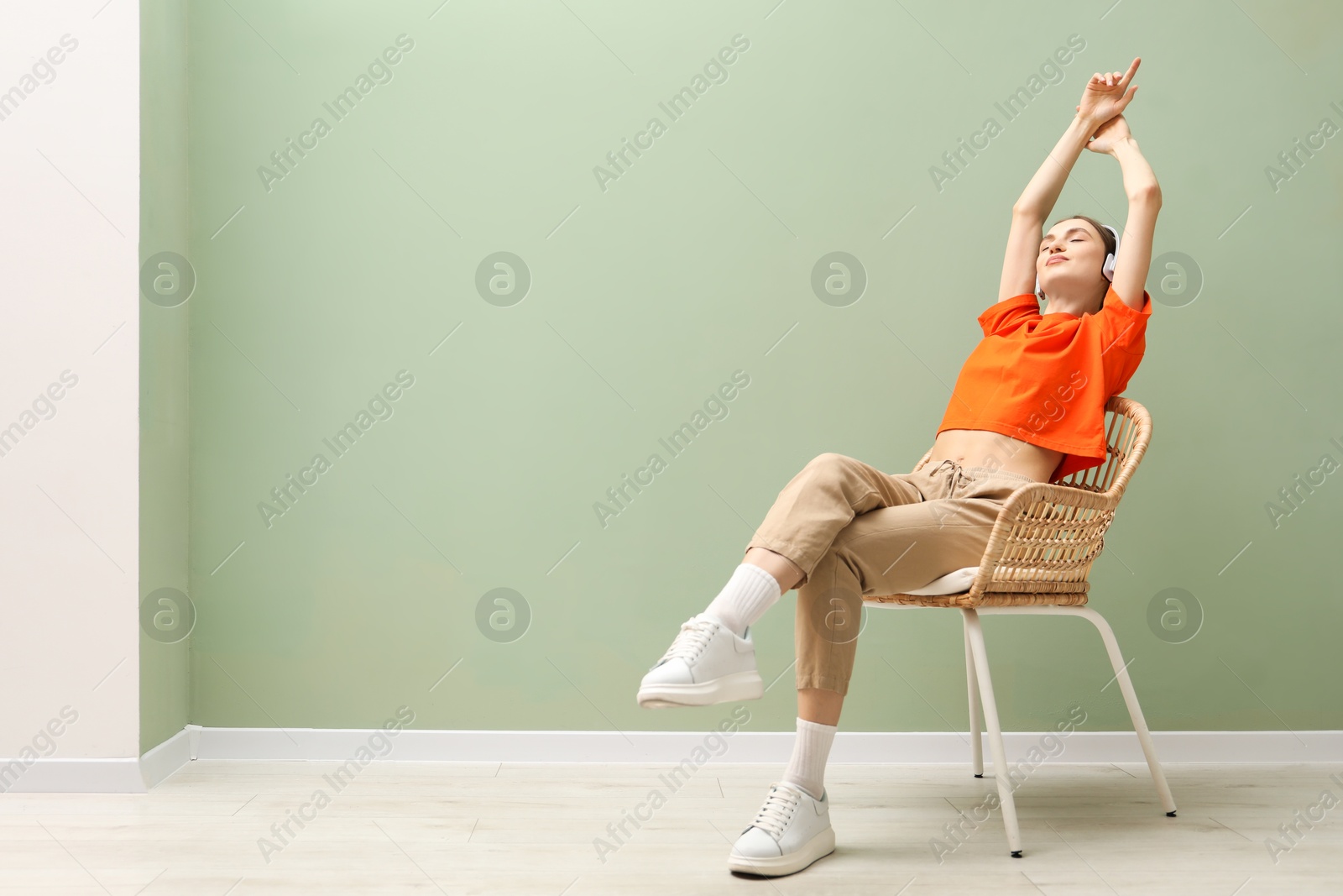 Beautiful woman with headphones relaxing in comfortable wicker armchair near pale green wall indoors, space for text Photo of Beautiful woman with headphones relaxing in comfortable wicker armchair near pale green wall indoors, space for text