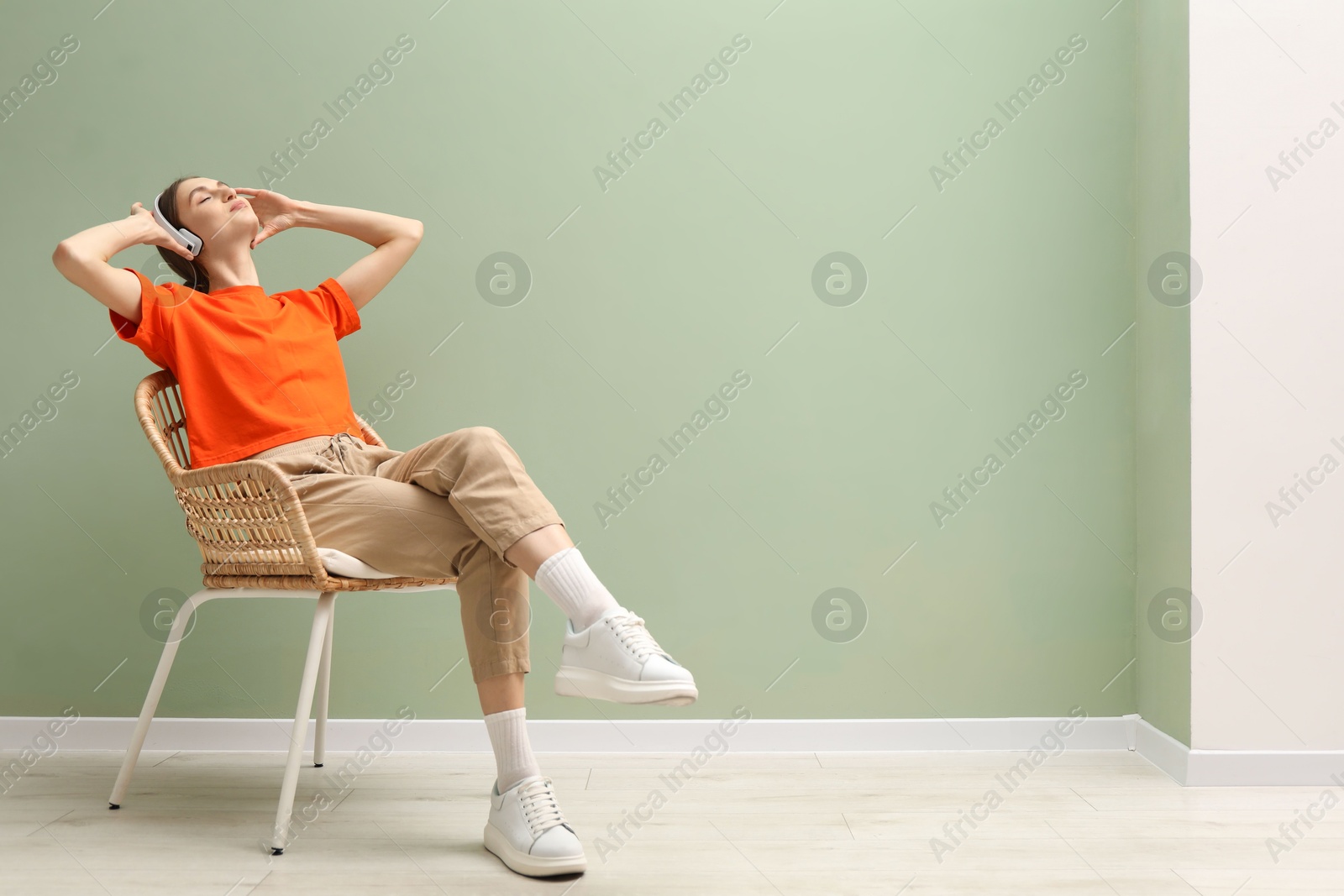 Beautiful woman with headphones relaxing in comfortable wicker armchair near pale green wall indoors, space for text Photo of Beautiful woman with headphones relaxing in comfortable wicker armchair near pale green wall indoors, space for text