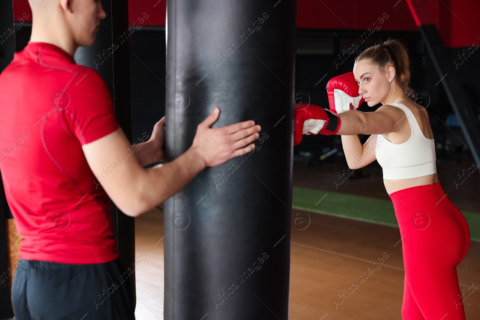 Boxing. Woman and her coach practicing with punching bag in training center Photo of Boxing. Woman and her coach practicing with punching bag in training center