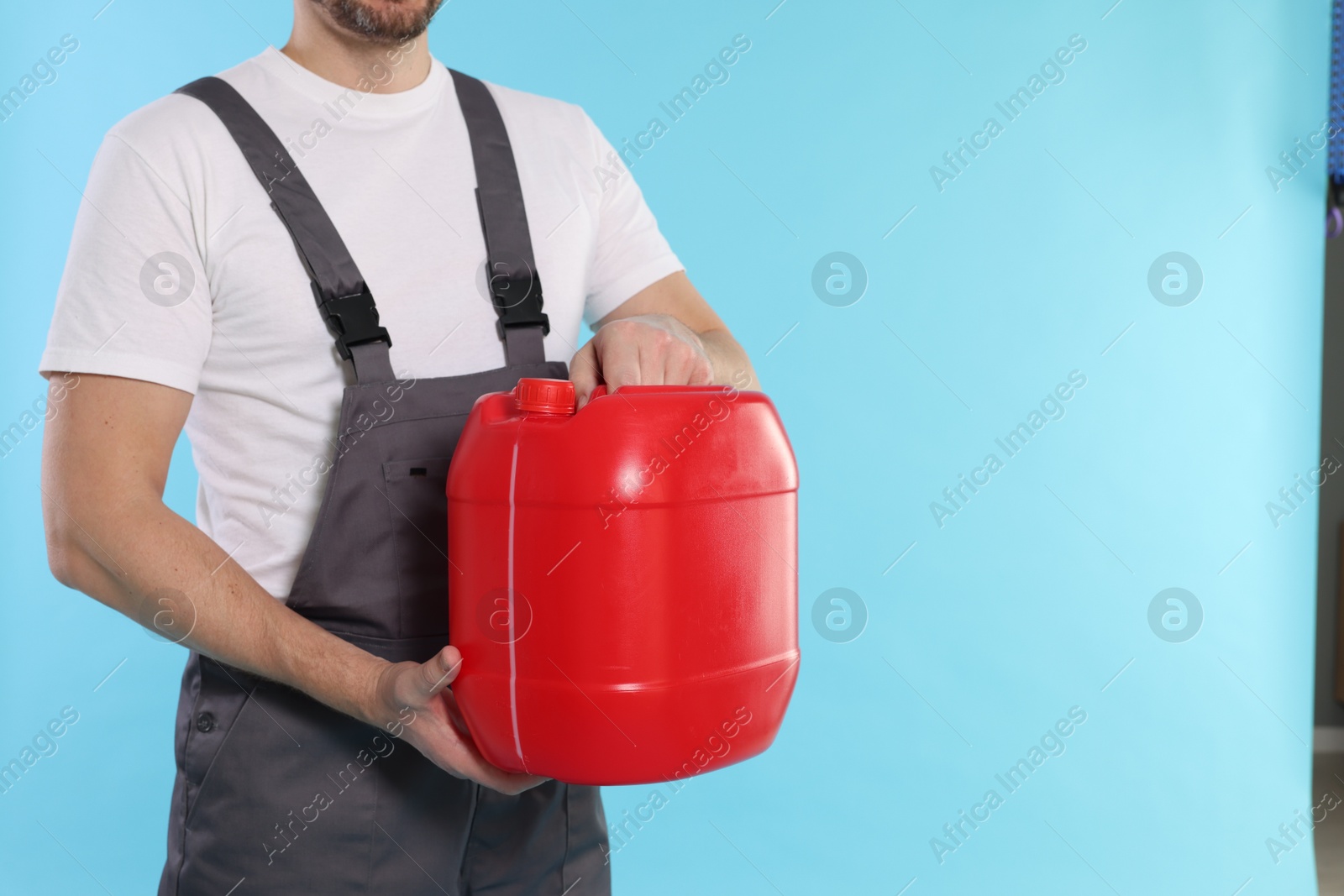 Man holding plastic canister on light blue background, closeup. Space for text Photo of Man holding plastic canister on light blue background, closeup. Space for text