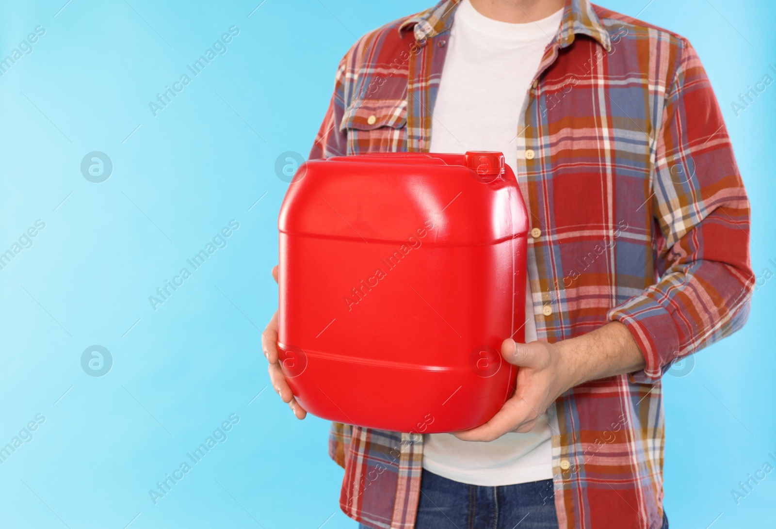 Man holding plastic canister on light blue background, closeup. Space for text Photo of Man holding plastic canister on light blue background, closeup. Space for text