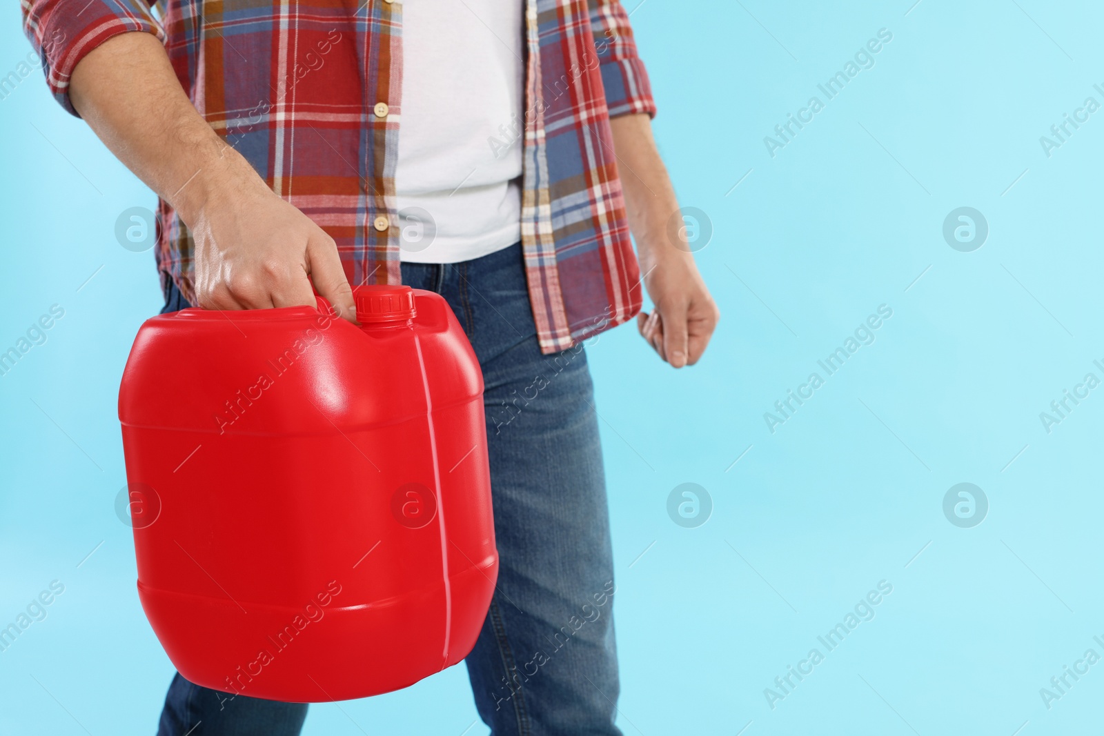 Man holding plastic canister on light blue background, closeup. Space for text Photo of Man holding plastic canister on light blue background, closeup. Space for text