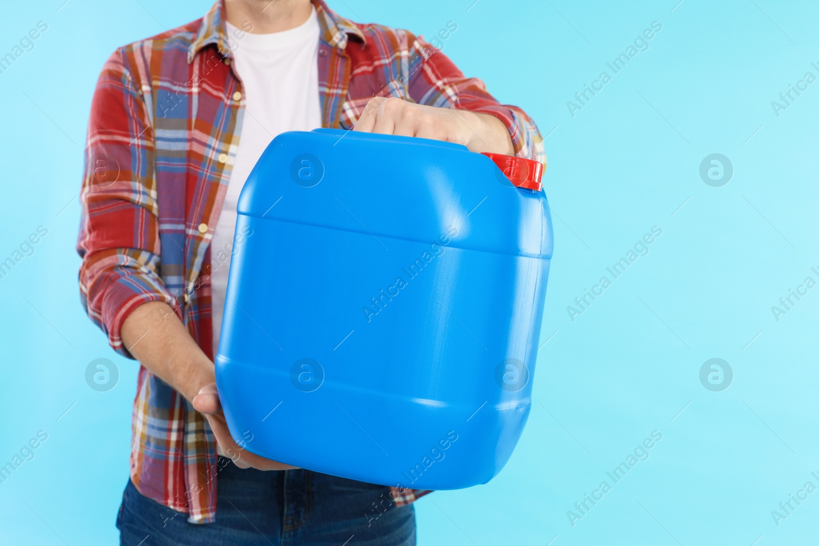 Man holding plastic canister on light blue background, closeup. Space for text Photo of Man holding plastic canister on light blue background, closeup. Space for text