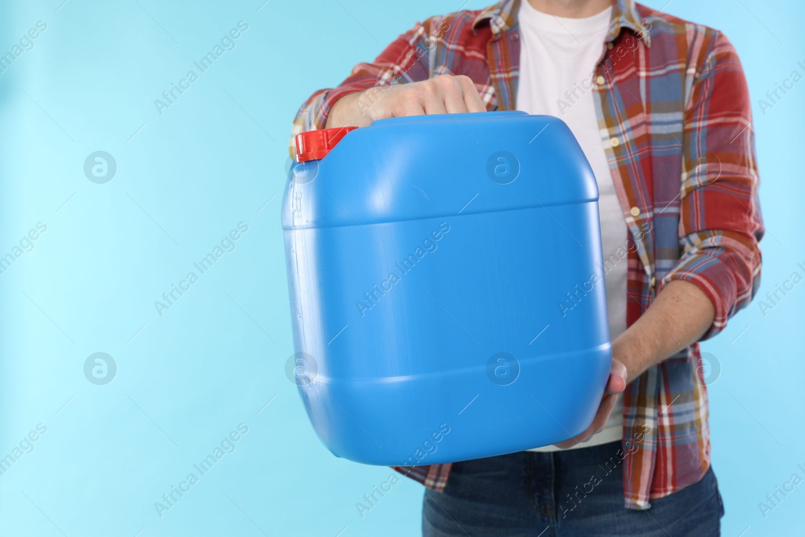 Man holding plastic canister on light blue background, closeup. Space for text Photo of Man holding plastic canister on light blue background, closeup. Space for text