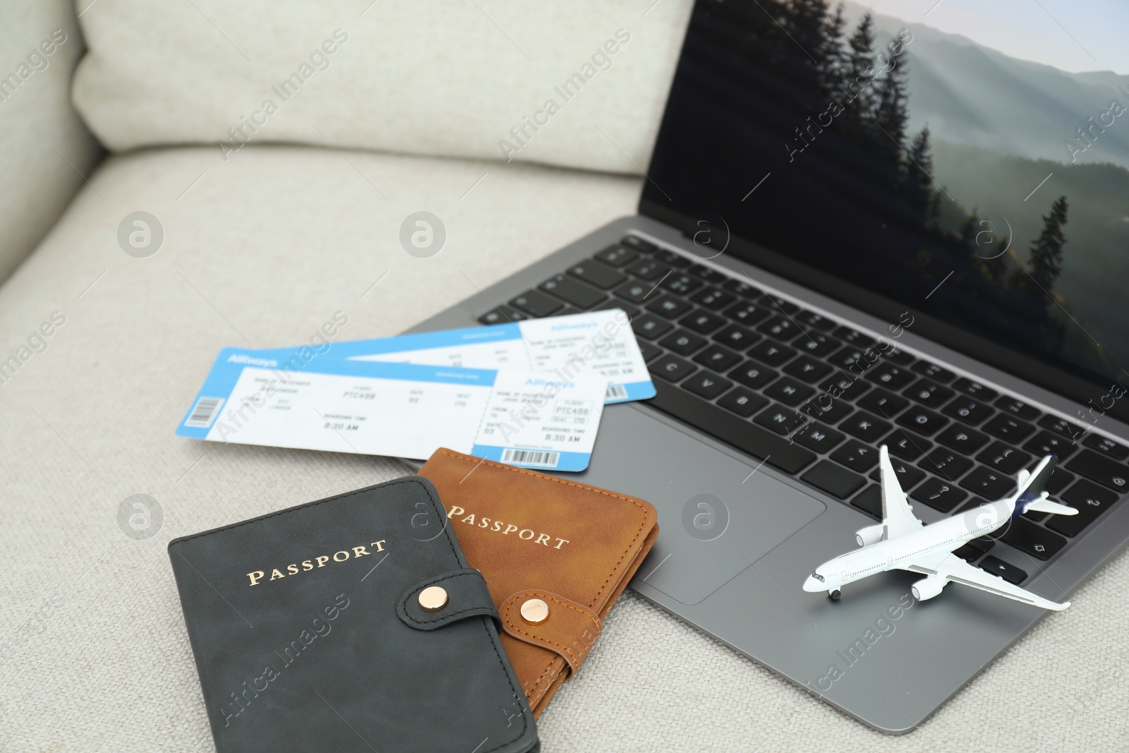 Passports, flight tickets, plane model and laptop on sofa, closeup Photo of Passports, flight tickets, plane model and laptop on sofa, closeup