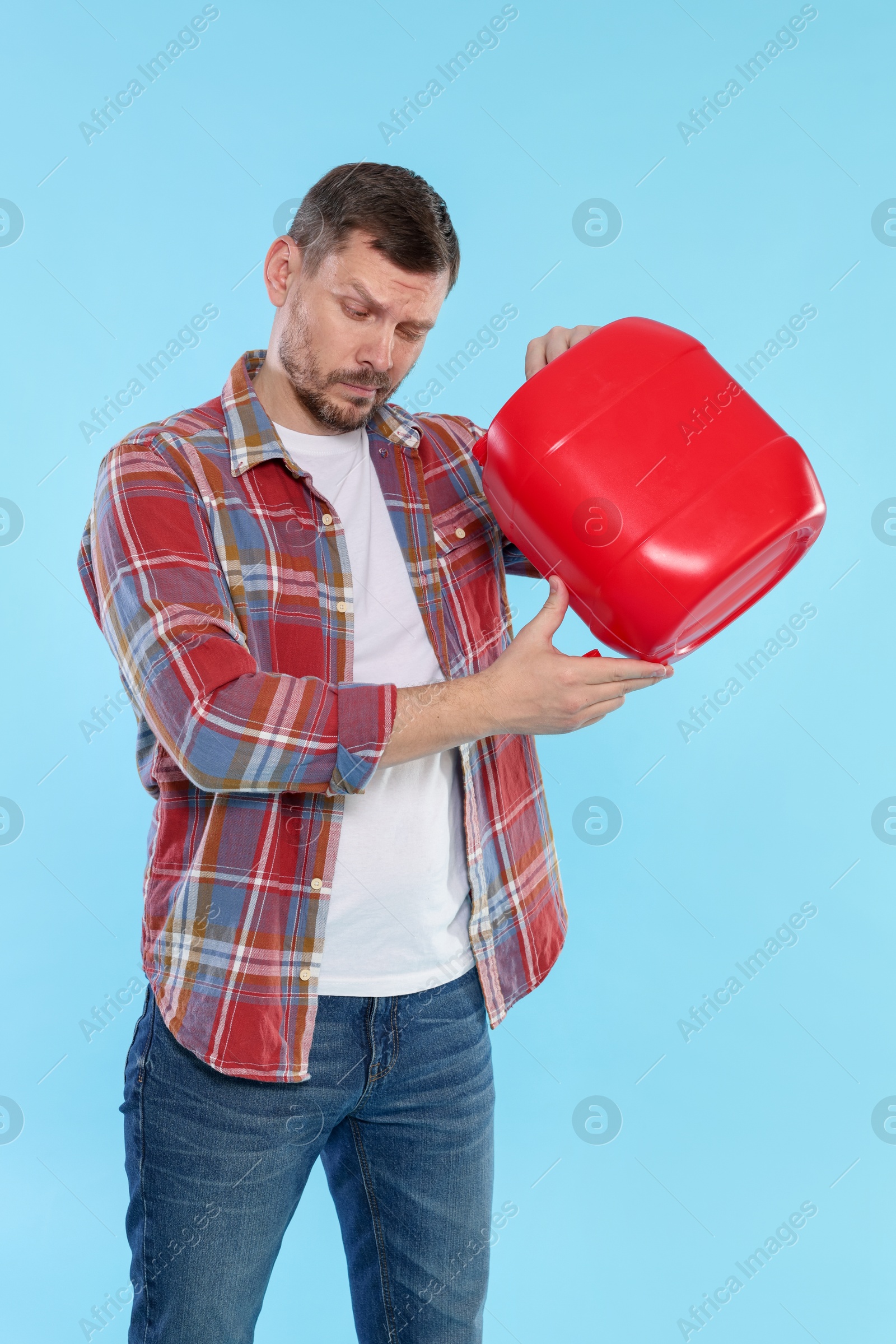 Man holding plastic canister on light blue background Photo of Man holding plastic canister on light blue background