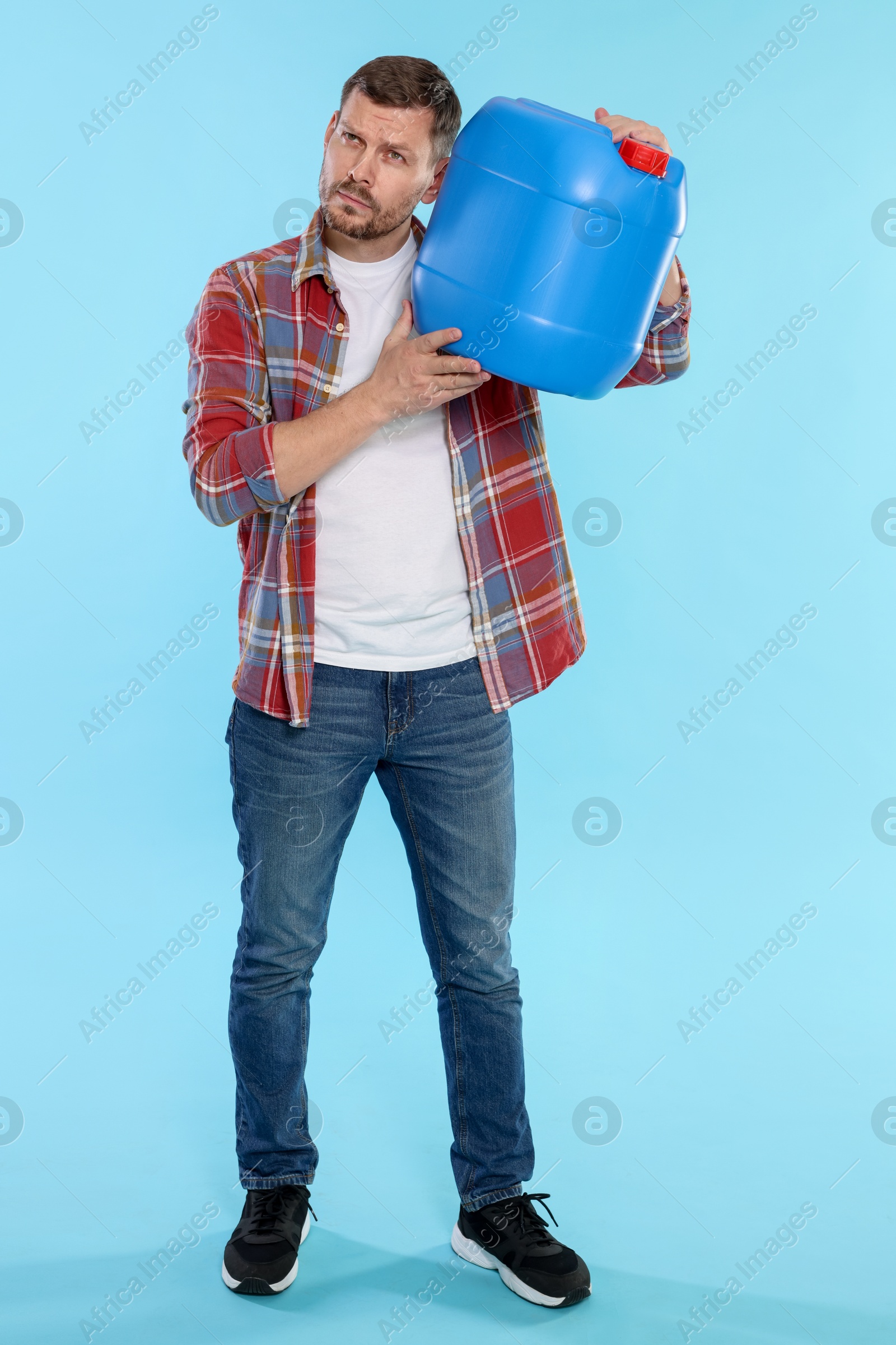 Man holding plastic canister on light blue background Photo of Man holding plastic canister on light blue background