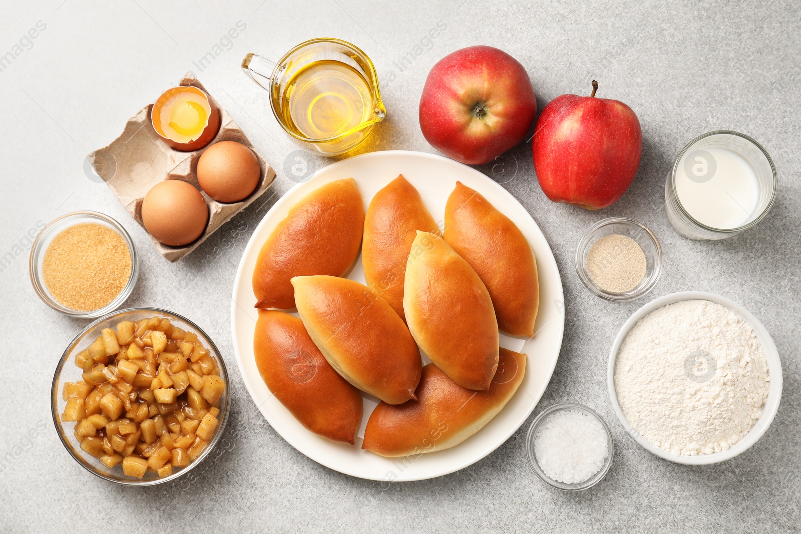 Tasty baked patties and ingredients on light grey table, flat lay Photo of Tasty baked patties and ingredients on light grey table, flat lay
