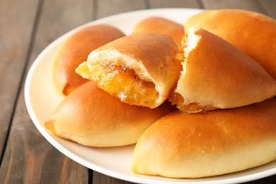 Photo of Tasty baked patties with orange jam on wooden table, closeup