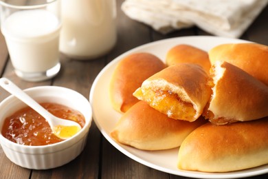 Photo of Tasty baked patties with orange jam on wooden table, closeup
