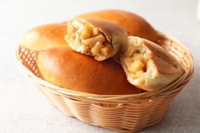 Photo of Tasty baked patties in wicker basket on light grey table, closeup