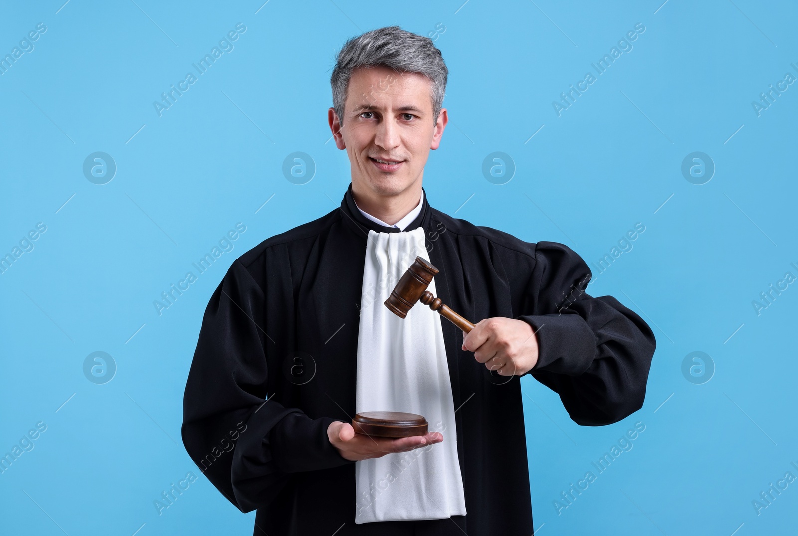 Smiling judge with mallet and sound block on light blue background Photo of Smiling judge with mallet and sound block on light blue background