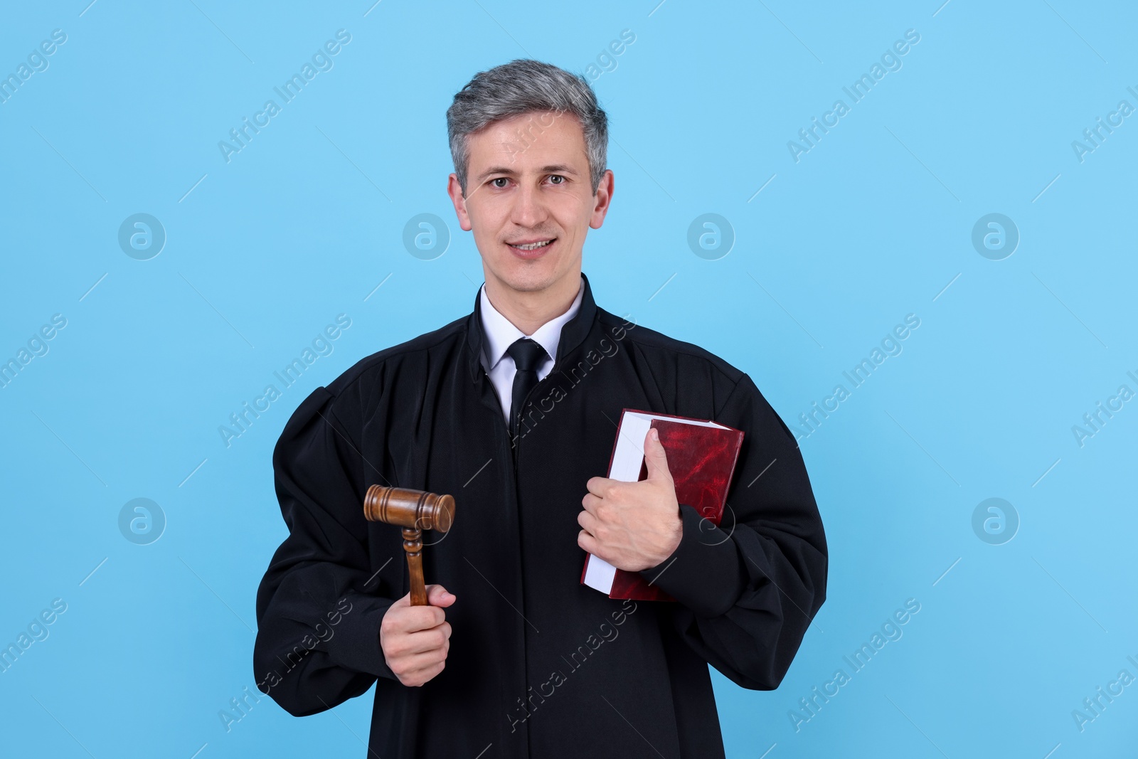 Smiling judge with mallet and book on light blue background Photo of Smiling judge with mallet and book on light blue background