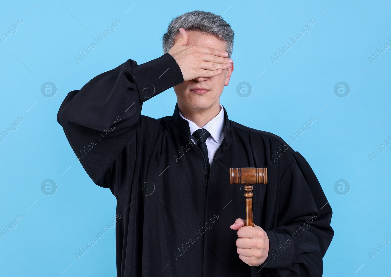 Photo of Judge with mallet covering eyes on light blue background