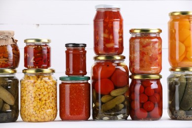 Photo of Many jars with different pickled products on white table