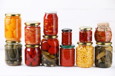 Photo of Many jars with different pickled products on white table