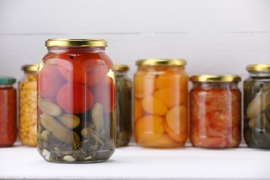 Photo of Many jars with different pickled products on white wooden table