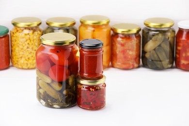 Photo of Many jars with different pickled products on white wooden table