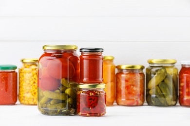 Photo of Many jars with different pickled products on white wooden table