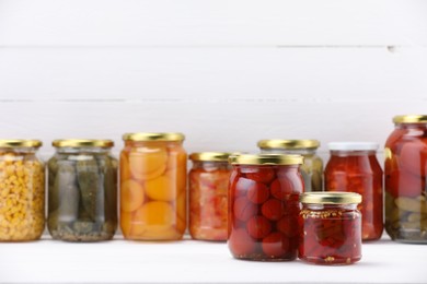 Photo of Many jars with different pickled products on white wooden table