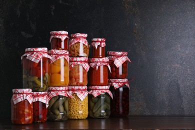 Photo of Many jars with different pickled products on wooden table, space for text