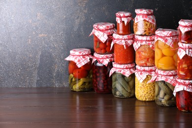 Photo of Many jars with different pickled products on wooden table, space for text