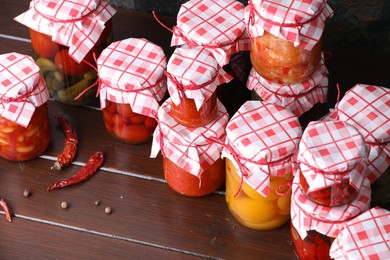 Photo of Many jars with different pickled products and ingredients on wooden table, above view
