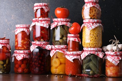 Photo of Many jars with different pickled products and ingredients on wooden table