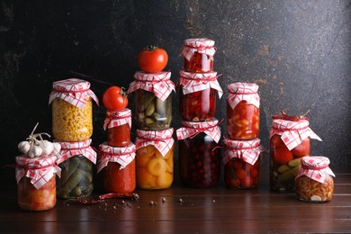 Photo of Many jars with different pickled products and ingredients on wooden table