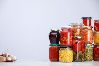 Photo of Many jars with different pickled products and ingredients on table against light grey background, space for text