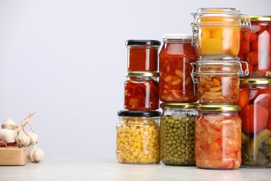 Photo of Many jars with different pickled products and ingredients on table against light grey background, space for text