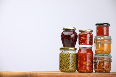 Photo of Many jars with different pickled products on wooden board against light grey background, space for text