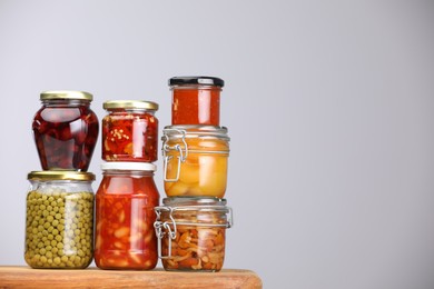 Photo of Many jars with different pickled products on wooden board against light grey background, space for text