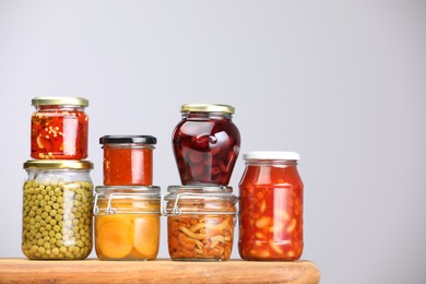 Photo of Many jars with different pickled products on wooden board against light grey background