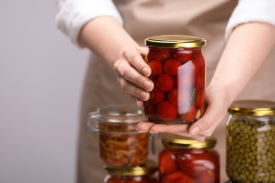 Photo of Woman with many jars of different pickled products on light grey background, closeup