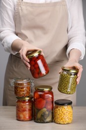 Photo of Woman with jars of different pickled products at wooden table against grey background, closeup