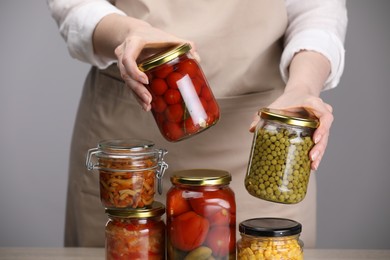 Photo of Woman with jars of different pickled products at table against grey background, closeup