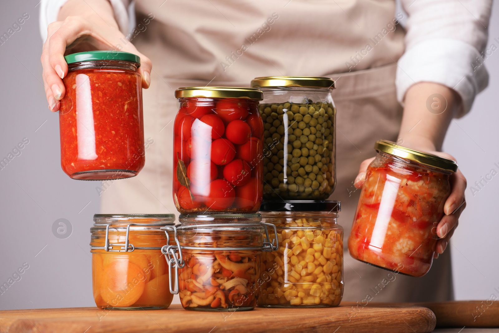Woman with jars of different pickled products at table against light grey background, closeup Photo of Woman with jars of different pickled products at table against light grey background, closeup