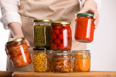 Photo of Woman with jars of different pickled products at table against light background, closeup