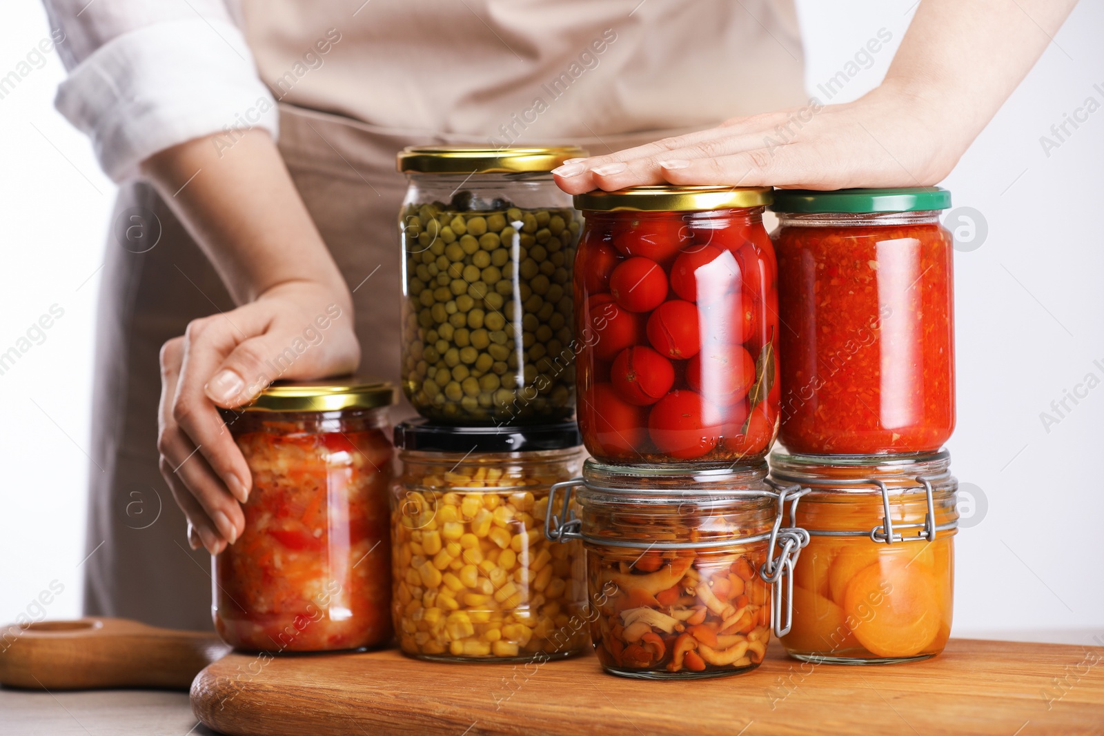Woman with jars of different pickled products at table against light background, closeup Photo of Woman with jars of different pickled products at table against light background, closeup