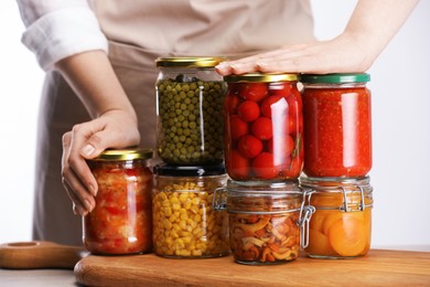 Photo of Woman with jars of different pickled products at table against light background, closeup